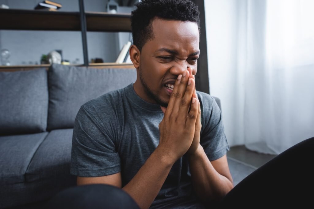 stressed african american man with hands together suffering from panic attack at home