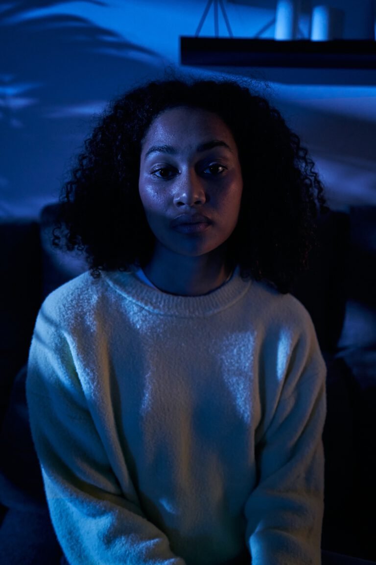 Vertical portrait young black woman sad look sitting alone at home in dark night. Female depressive.